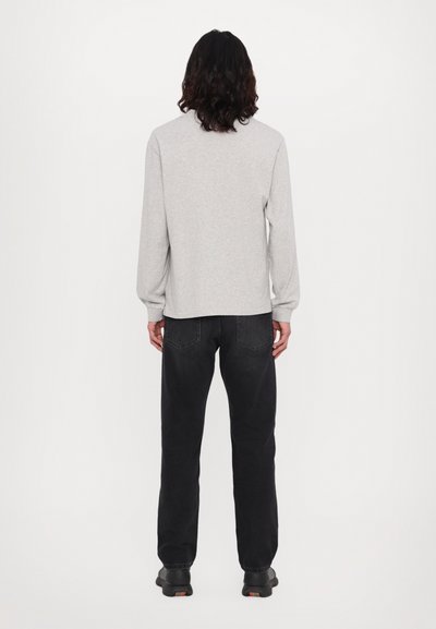 Gray long-sleeve shirt with a relaxed fit, paired with black jeans. The fabric appears soft, and the shirt features a rounded hem and cuffed sleeves.