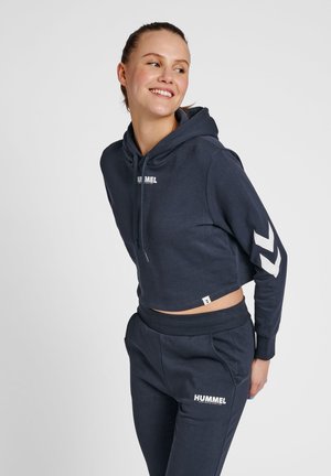 Marineblå cropped hoodie og matchende joggers, begge i blødt bomuld, med hvid logo og chevron-design på ærmerne samt ribbede manchetter.