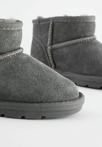 Graue Wildleder-Stiefeletten mit glatter Textur, runder Zehenform und kontrastierenden Garnverzierungen am Schaft und der Sohle. Flache Gummisohle.