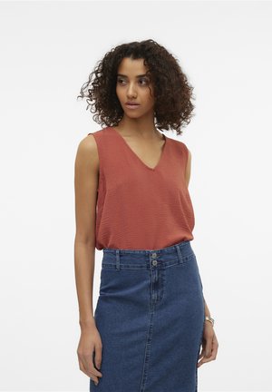 V-hals, mouwloze top in gestructureerde roestkleurige stof, gecombineerd met een mid-length blauwe denimrok met een split aan de voorkant en tweeknoopsluiting.