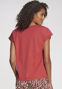 Hnedooranžové tričko s krátkym rukávom a voľným strihom, s okrúhlym výstrihom. Mäkký materiál s prehnutými rukávmi a čistými detailmi šitia.