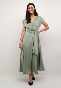 Satin wrap dress in soft green, featuring short sleeves, a belted waist, and flowing skirt. Textured fabric with smooth finish.