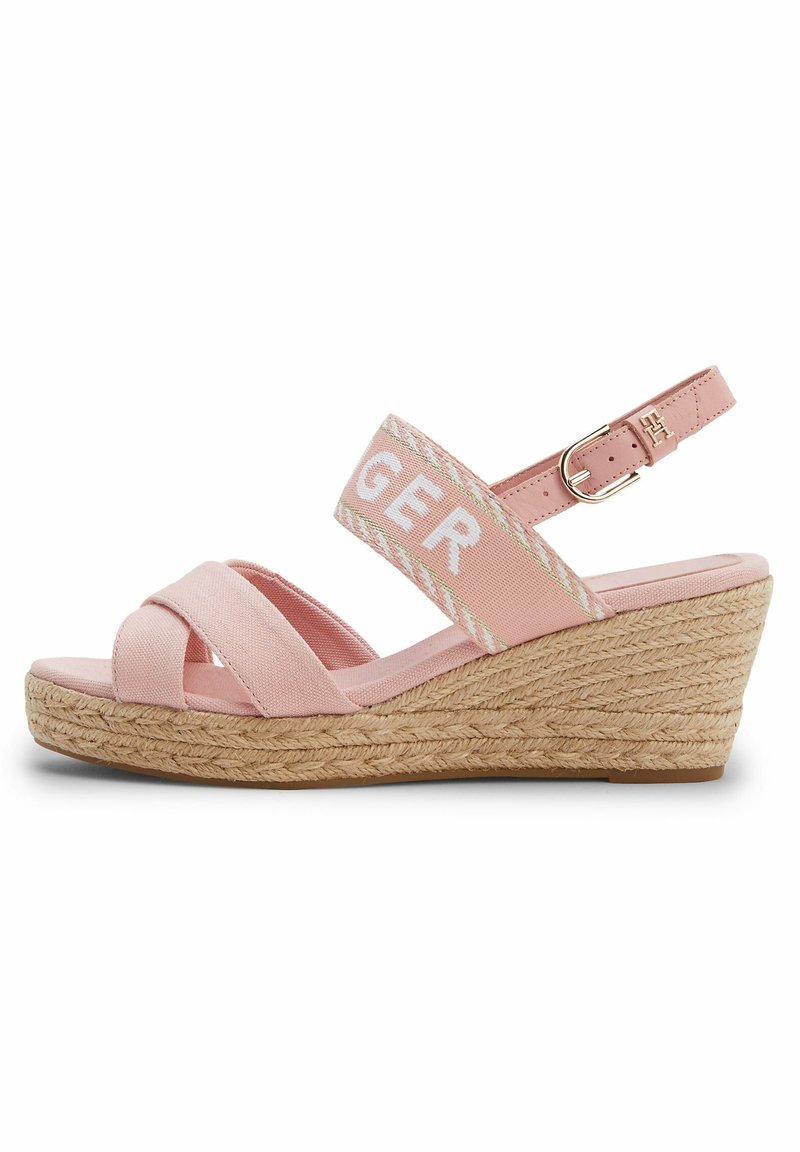 Sandale compensée rose avec semelle en jute tissée, brides croisées en tissu aux orteils, bride de cheville ajustable avec boucle dorée, et bande élastique siglée.