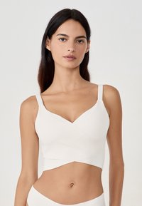 Bralette bianca a strati con scollatura a V, spalline regolabili e design senza cuciture. Tessuto morbido e finitura liscia con stile avvolgente.