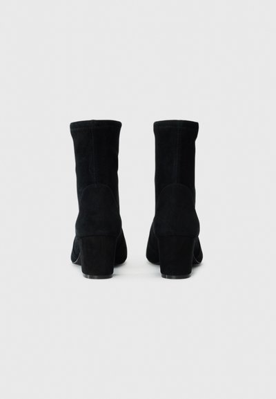 Botine negre din suede, cu o textură netedă, toc rotund și un design de înălțime medie. Prezintă o siluetă simplă și detalii de cusătură minime.