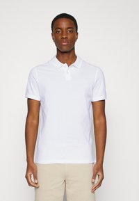 Hvit polo skjorte laget av bomull, med klassisk krage og to-knappers placket, korte ermer og en fitted design. Glatt tekstur.