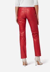 Rode leren broek met een gladde textuur en een rechtmodel ontwerp, gedragen met lichtbeige hoge hakken. Zichtbare stiksels langs de naden.