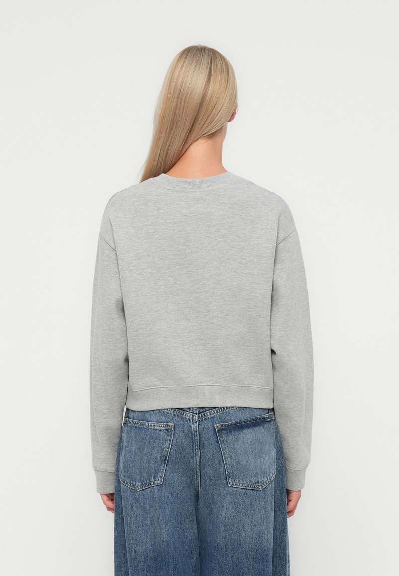 Grijze sweatshirt met een ronde hals, geribbelde manchetten en een cropped fit, gecombineerd met losse blauwe denim jeans. De stof lijkt zacht en gestructureerd.
