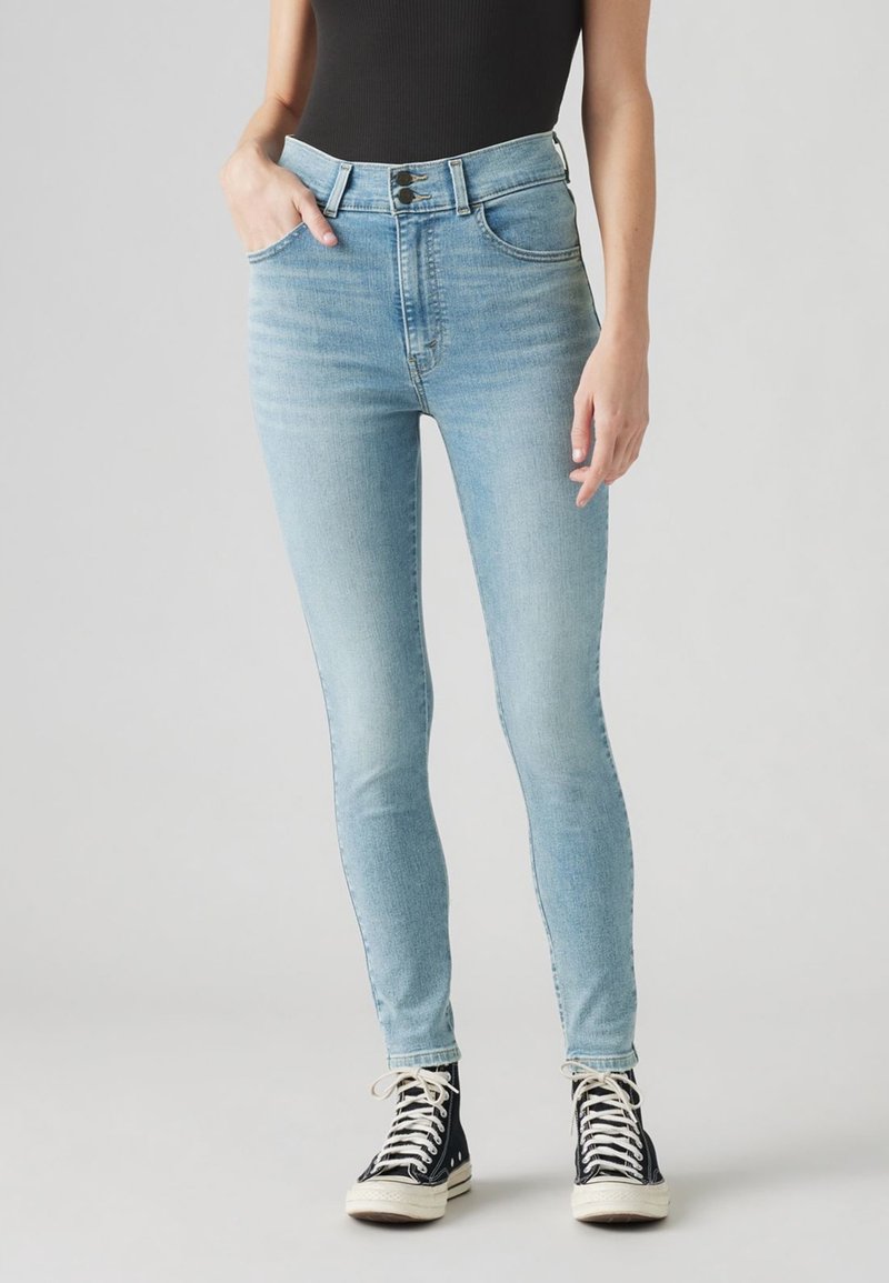 Jean taille haute bleu clair avec une coupe slim, dotés de poches avant et d'une fermeture à deux boutons, associés à des baskets montantes noires.