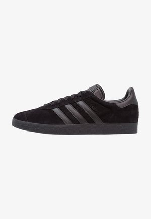 Baskets Adidas en daim noir avec trois bandes en cuir noir, lacets noirs et semelle en caoutchouc texturée noire, vues de côté.