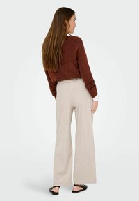 Un pull en tricot marron, un pantalon large côtelé beige, et des sandales noires. Le pull a une coupe ample ; le pantalon présente une taille haute et des rayures verticales.