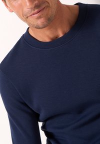 Felpa a maniche lunghe blu navy con scollatura rotonda. Il materiale appare liscio con una consistenza morbida e senza motivi o dettagli visibili.