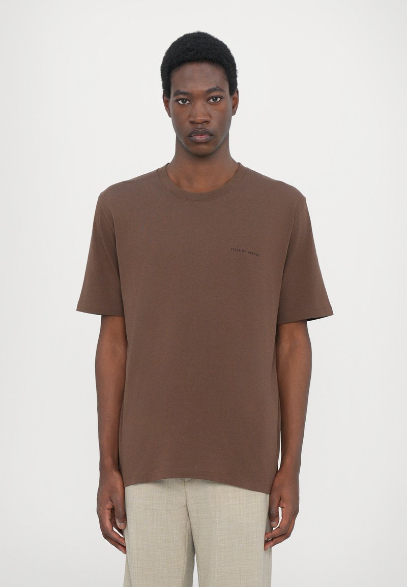 Brown cotton t-shirt with short sleeves, a round neckline, and a small printed logo on the chest; relaxed fit and soft texture.