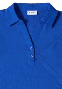 Polo bleu vif avec col, deux boutons bleus sur la patte, manches courtes et une étiquette blanche portant la mention "Cecil" à l'intérieur du col.