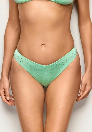 Kobieta nosząca jasnospodnie bikini w kolorze zielonym z małymi ozdobami z cyrkonii, widoczna od talii do górnej części ud.