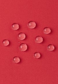 Sfondo di tessuto rosso con gocce d'acqua di varie dimensioni, chiaramente visibili. La trama del tessuto mostra un motivo intrecciato sotto le gocce.