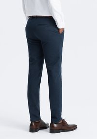 Chinos blu navy con vestibilità slim, realizzati in tessuto leggero, con una tasca posteriore con dettaglio a bottone, indossati con scarpe in pelle marrone.