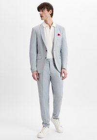 Hellgrauer Anzug aus strukturiertem Stoff, einreihige Jacke und passende Hose. Kombiniert mit einem weißen Polohemd und weißen Sneakers.