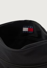 Sort stofpose med lynlåslukning, der har en "TOMMY JEANS" label indeni. Glat tekstur og et minimalistisk design.