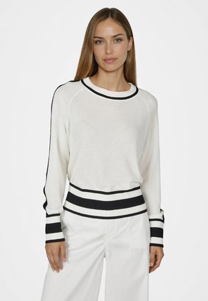 Woman wearing a white sweater with black stripes on collar, cuffs, waistband, and pants, posing against a plain white background.