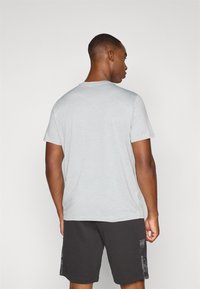 Grå t-skjorte med kort erm laget av bomull, kombinert med mørke shorts med et mønstret sidepanel. Glatt tekstur, standard passform.