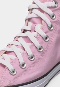 Ροζ πάνινο αθλητικό παπούτσι με λευκά κορδόνια περασμένα από μεταλλικά κρικάκια και λευκή λαστιχένια σόλα με μαύρο περιθώριο.