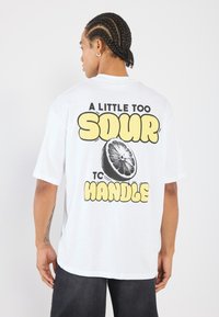Hvid bomulds T-shirt med grafisk print af en skivet citron og tekst: "LIDT FOR SUR AT HÅNDTERE" i sort og gul. Korte ærmer.