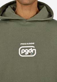 Felpa verde oliva con un grande logo bianco con il testo "PEGADOR" sopra "pgdr" in un contorno arrotondato. Tessuto di cotone morbido e strutturato.