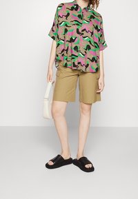 La maglietta a maniche corte presenta un motivo multicolore di scarpe con tacco su uno sfondo scuro. Abbinata a pantaloni cargo beige e sandali neri.