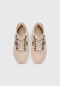 Para beżowych i brązowych sneakersów z teksturowaną tkaniną i białymi sznurówkami, widziana z góry na jednolitym jasnym tle.