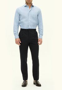 Helles blaues Hemd mit Knöpfen und einer Brusttasche, kombiniert mit dunklen, taillierten Hosen und schwarzen Slippern. Glattes Material, strukturierte Passform.