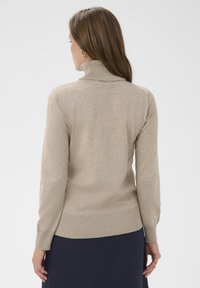 Pull à col roulé beige avec poignets et ourlet côtelés, texture lisse et coupe ajustée, vu de dos.