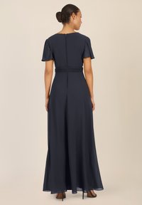 Vestido maxi azul marino con mangas cortas y con volantes, cintura ceñida y cierre de cremallera en la parte posterior. Tejido suave y fluido con una capa transparente.