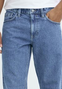 Lyseblå denimjeans med rette ben, fem-lomme design og metallknapplukking; stoffet viser et teksturert kornmønster.