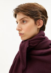 Écharpe en tricot violette enroulée autour du cou, mettant en valeur un tissu texturé avec un design ample et drapé. Apparence douce et chaude et couleur profonde.