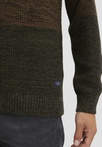 Maglione a maglia testurizzata con strisce verde scuro e marrone. Polsini e orlo a costine. Presenta un piccolo etichetta tessuta sul lato sinistro in basso.
