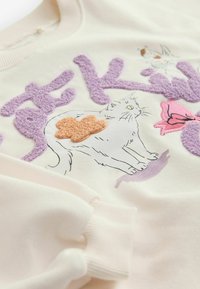 Felpa color crema chiaro con ricami testurizzati viola, rosa e arancioni raffiguranti un gatto e fiori, con polsini e collo a costine.