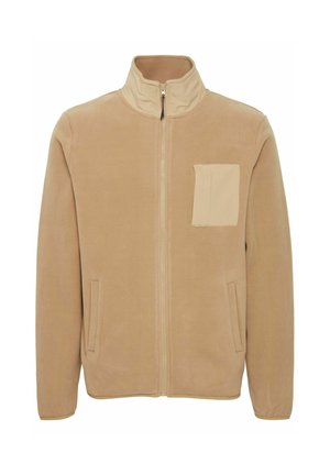 Veste en polaire beige avec un col montant, fermeture éclair à l'avant, poches latérales et une poche poitrine carrée dans une teinte légèrement plus claire. Texture douce.