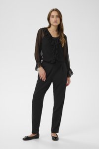 Blusa nera con fronte arricciato e maniche trasparenti, abbinata a pantaloni neri su misura e ballerine nere lucide. Design semplice ed elegante.