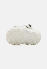 Shoe branco de borracha com uma sola texturizada, apresentando um design arredondado e detalhes em preto, incluindo uma decoração temática desportiva.