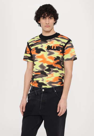 Korte mouwen camo t-shirt in neon oranje, groen en zwart met een gestructureerd "BLUE" logo op de borst, gecombineerd met zwarte denim jeans.