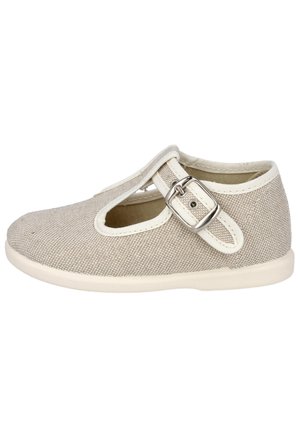 Zapato beige para niño pequeño con tela texturizada, borde blanco y una correa con hebilla plateada sobre la parte superior, suela plana, vista lateral.