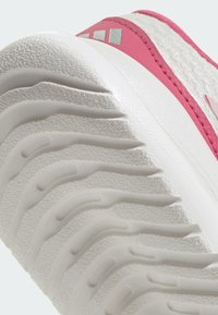 Gros plan d'une semelle blanche texturée de sneaker avec des rainures profondes et un bord supérieur rose avec un logo partiellement visible.