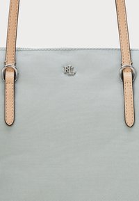 Saco tote azul-claro feito de material texturizado, apresentando alças em pele bege, ferragens prateadas e um logótipo discreto no centro.