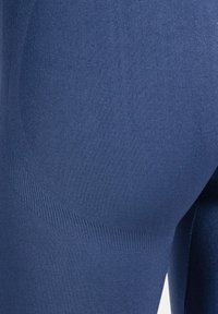 Nahaufnahme eines Beins einer Person, die enge, strukturierte, dunkelblaue Sportleggings trägt.