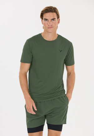 Young man with light brown hair wearing a matching green athletic t-shirt and shorts with black compression shorts underneath.