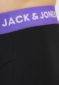 Schwarze Herren-Boxershorts mit einem lila elastischen Bund, der mit weißer "JACK & JONES" Schrift versehen ist. Glatte Textur und eng anliegendes Design.