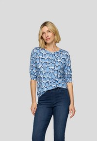 Bluse mit blauem abstraktem Muster, Rundhalsausschnitt und Dreiviertelärmeln, kombiniert mit dunkelblauen Jeans. Glattes Material mit lockerer Passform.