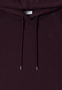 Bordeauxfarbener Kapuzenpullover aus weichem Stoff. Verfügt über eine Kängurutasche, Kordeln mit Metallspitzen und ein kleines, geprägtes Logo.