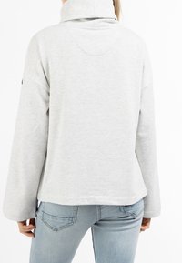 Sudadera de color gris claro con cuello alto, hombros caídos y mangas largas. Tejido suave, corte relajado y dobladillo redondeado en la parte posterior.